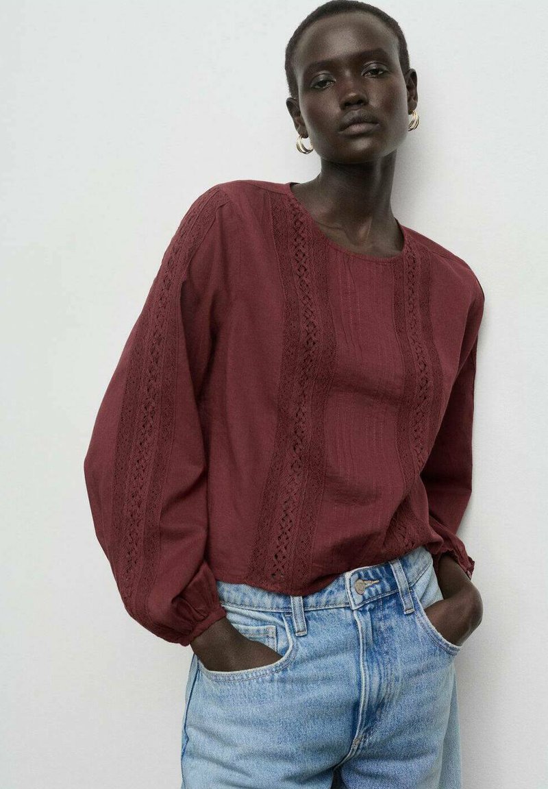 Blusa burdeos de manga larga con rayas verticales texturizadas y acentos de encaje, combinada con vaqueros de mezclilla de lavado claro. Tejido suave y corte relajado.
