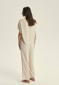 Luźny, kremowy zestaw odzieży domowej wykonany z miękkiego materiału, składający się z szerokiego topu z krótkim rękawem oraz prostych spodni, o minimalistycznym wzornictwie.
