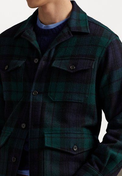 Sötétzöld és tengerészkék kockás flanel ing, két mellzsebbe, csúcsos gallérral és fekete gombokkal. Puha anyagú és normál szabású.