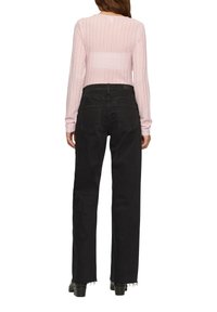 Roze geribbelde langslavige top met een ronde hals, gecombineerd met hoge zwarte jeans met achterzakken en rafelige zoom.