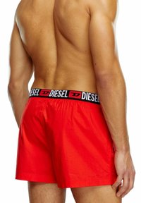 Rode zwembroek van lichtgewicht, gladde stof. Heeft een zwarte tailleband met grote "DIESEL" lettering. Middelste dijlengte, elastische rek.