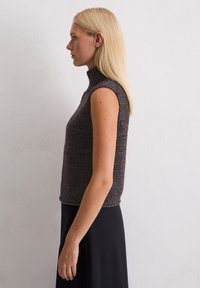 Grijze mouwloze coltrui met een gestructureerde brei, met een slim fit en ribbeldetails, gecombineerd met een zwarte rok.