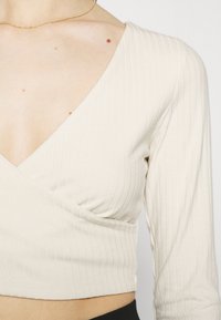 Hellbeiges, geripptes Langarmshirt mit tiefem V-Ausschnitt und Wickeldesign, das eine glatte Textur und eine figurbetonte Silhouette aufweist.