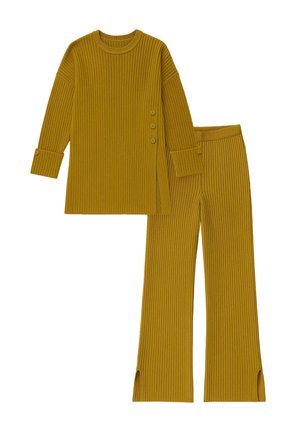 Set od rebrastog pletiva u senfu žutoj boji, koji se sastoji od dugih rukava s bočnim dugmadi i suženih hlača s bočnim prorezima na člancima.
