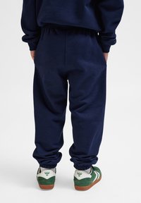 Pantaloni della tuta navy con vita e polsini elastici, dotati di un taglio rilassato. Abbinati a sneakers verdi e bianche con un branding discreto.