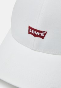 Hvit bomull baseball cap med rødt brodert Levi's-logo på forsiden. Strukturert design med buet skjerm og sømdetaljer.