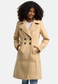 Dubbelzijdige beige wollen jas met grote zwarte knopen, geknipte kraag, zijzakken en subtiele stikdetails.