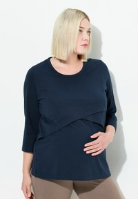 Marineblaues langärmliges Stilloberteil mit geschichteter Gestaltung, weichem Material, rundem Halsausschnitt und lockerer Passform, getragen über beigen Leggings.