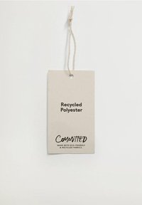 Genanvendt polyesteretiket, lysebeige farve med tekstureret overflade. "Committed" trykt i sort, hvilket angiver brug af miljøvenlige materialer.