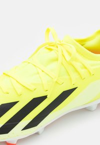 Crampons de football jaune vif avec des rayures noires accentuées, matériau synthétique léger, tige texturée et conception de fermeture à lacets traditionnelle.