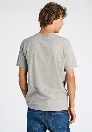 Grå kortermet t-skjorte med rund hals, laget av en myk bomullsblanding, vist på en person som står med ryggen til, kombinert med blå jeans.