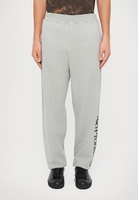 Pantalones de chándal grises con un ajuste holgado, cintura elástica y detalle impreso de "NO PROBLEM" en negro a lo largo de la pierna izquierda. Textura suave y lisa.