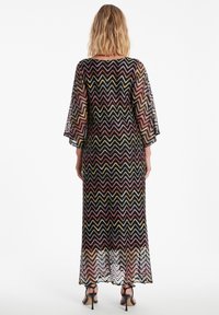 Lang, doorschijnend jurkje met een zigzagpatroon in multikleurige draden. Heeft klokmouwen en een gegolfde zoom. Ggedragen met sleehakken.