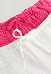 Twee gelaagde rokken met een roze bovenlaag en een witte onderlaag. Gemaakt van een textuurstof met geplooide tailles en gestrikte strikken.