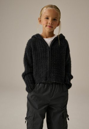 Schwarze, strukturierte Zip-Hoodie mit Kapuze und Rippendesign; kombiniert mit lockeren schwarzen Cargo-Hosen mit Taschen und elastischem Bund.