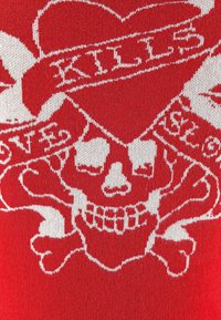 Roter Strickstoff mit einem weißen Totenkopf und gekreuzten Knochen-Motiv, das ein Herz und das Wort "KILLS" in das Muster integriert.