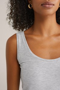 Grå scoop-neck linne tillverkat av ett mjukt, texturerat material. Har breda axelremmar och en slät, figursydd silhuett. Guldörringar.