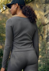 Haut à manches longues gris côtelé avec une coupe décontractée, associé à un legging côtelé assorti. Une casquette noire est portée, mettant en valeur la tenue.