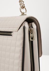 Jasnoróżowa pikowana torebka z eko skóry z srebrnymi elementami, wyposażona w górny zamek błyskawiczny i czarne wykończenia wzdłuż krawędzi. W zestawie łańcuszkowy pasek.