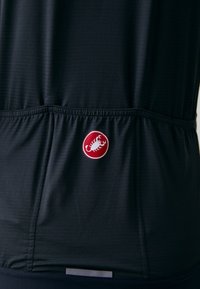 Svart atletisk topp med teksturert stoff. Har en rød logo med et skorpionemblem ved midjen og en elastisk nederkant for en sikker passform.