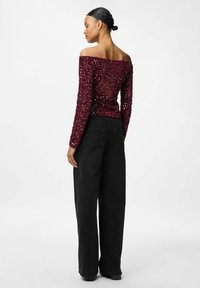 Bordeaux off-shoulder top med palietter og lange ærmer, parret med sorte vide bukser, der fremhæver en struktureret overflade og tætsiddende design.