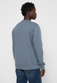Felpa grigia in cotone con collo rotondo, polsini e fondo a coste, caratterizzata da una texture liscia e un design minimalista, mostrata dalla parte posteriore.