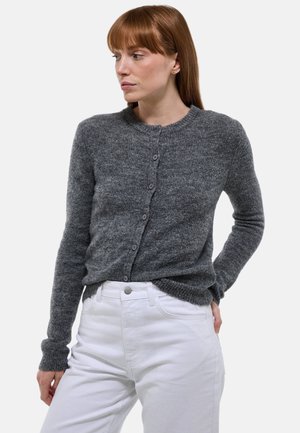 Un cardigan en tricot gris avec un col rond, une fermeture à boutons et des poignets côtelés. Porté par-dessus un pantalon blanc, mettant en valeur un tissu texturé.