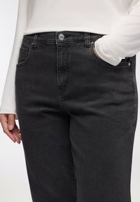 Czarne dżinsy o średnim stanie, z pięcioma kieszeniami, metalowymi akcentami i gładką teksturą. Projekt jest klasyczny i dopasowany.