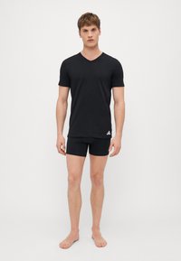 Schwarzes V-Ausschnitt-T-Shirt und passende Shorts aus weichem Stoff. Mit einem kleinen weißen Logo am linken Saum des Shirts.