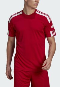 T-shirt sportivo rosso in tessuto traspirante, con strisce bianche sulle spalle e logo Adidas sul manico. Maniche corte, scollatura rotonda.