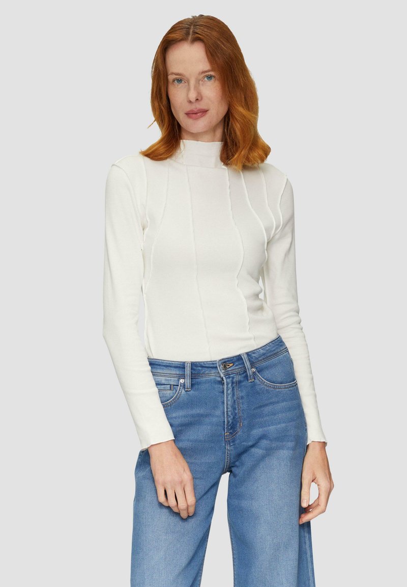 Un turtleneck blanc à manches longues avec des coutures verticales, associé à un jean taille haute bleu clair. Texture lisse et ajustée, design minimaliste.