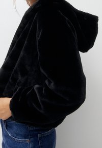 Czarna krótka bluza z kapturem, uszyta z miękkiego, pluszowego materiału, o luźnym kroju, z szerokimi rękawami i gładką fakturą.
