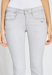 Jeans de denim de color gris claro con un ajuste slim, que presentan un cierre de botón, bolsillos frontales y detalles de costura sutiles. Etiqueta de la marca visible en el bolsillo.