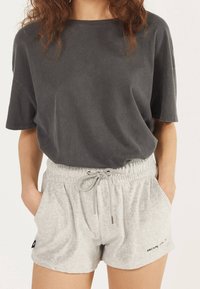 Graues Baumwoll-T-Shirt mit kurzen Ärmeln, kombiniert mit hellgrauen Shorts mit Kordelzug, Seitentaschen und Logodetail am Saum.