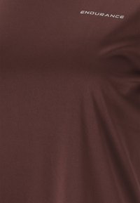 Burgundy t-shirt i mjukt tyg, med ordet "ENDURANCE" tryckt i vitt på övre vänstra sidan. Slät yta.