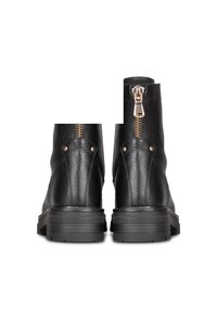 Botas de tobillo de cuero negro con un acabado texturizado, un cierre de cremallera dorado y una suela de goma negra resistente. La vista trasera muestra costuras dobles.