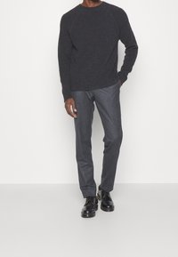 Dunkelgrauer gestrickter Pullover mit Rundhalsausschnitt, kombiniert mit maßgeschneiderten, anthrazitgrauen Hosen und schwarzen Schnürschuhen. Einfaches Design und einfarbige Farben.