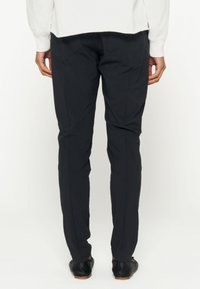 Schwarze maßgeschneiderte Hose mit schmalem Schnitt, ausgestattet mit Gesäßtaschen und einer glatten Textur, kombiniert mit schwarzen Schuhen und einem weißen Oberteil.