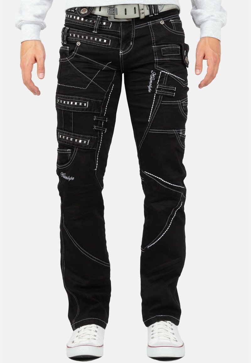 Pantaloni cargo neri con cuciture bianche, caratterizzati da numerose tasche e dettagli con cinghie. Realizzati in tessuto di denim con taglio dritto.