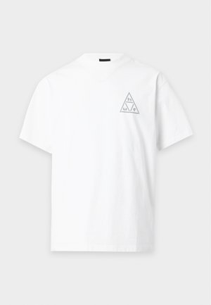Biały t-shirt z krótkim rękawem z małym szarym trójkątnym logo zawierającym litery na górnej lewej części klatki piersiowej na jednolitym tle.