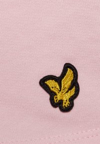 Tecido rosa com um logotipo de borboleta dourada bordada e contornado a preto. A textura é suave e a costura é detalhada.