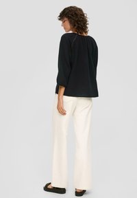 Czarna, teksturowana bluzka z rękawami 3/4, w luźnym kroju, zestawiona z kremowymi spodniami o szerokiej nogawce i czarnymi sandałami na platformie. Prosty design, bez wzorów.