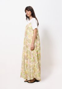Maxikleid aus leichtem Stoff mit einem floralen Muster in Pastellfarben. Kurze weiße Ärmel, fließendes Design und flache Sandalen.
