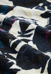 Tissu froissé avec des motifs abstraits de coups de pinceau noirs, blancs, bleus et violets formant des formes irrégulières et des contrastes dynamiques.