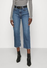 Höga blå denimcroppade jeans med rak passform, slitna fållar och svart bälte med metallbeslag. Randig långärmad topp.