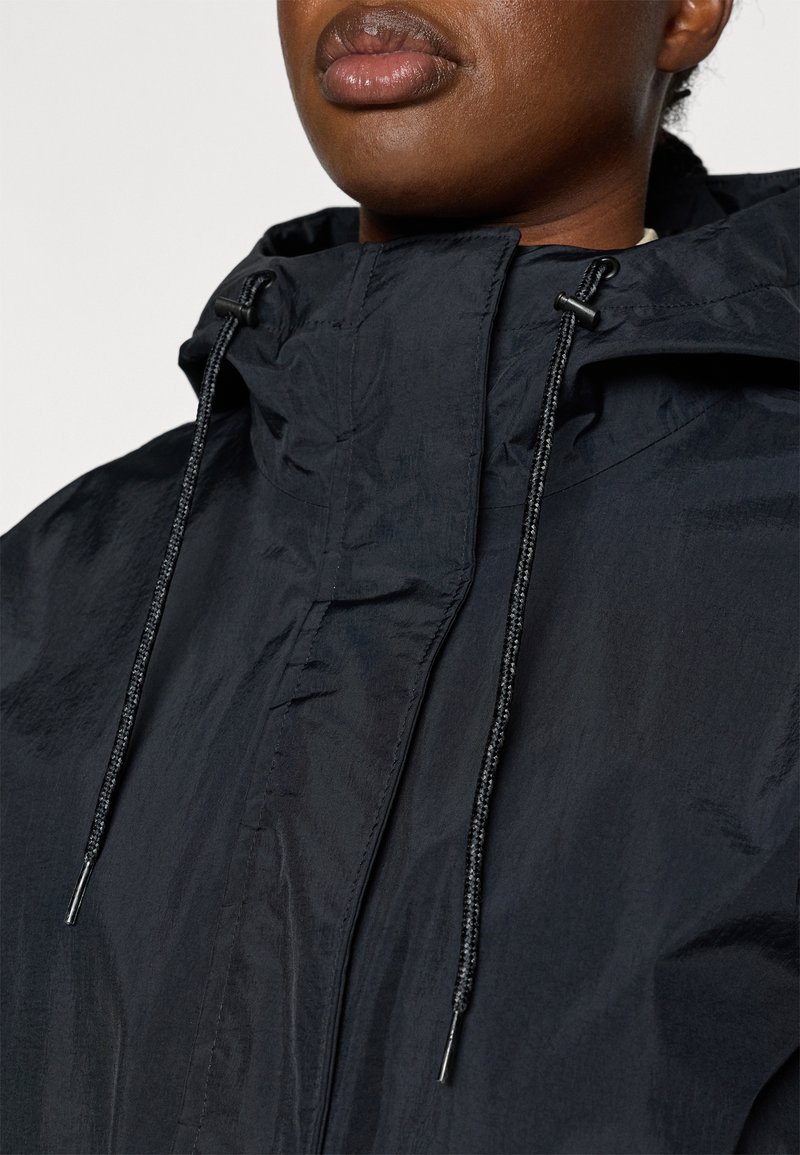 Veste légère noire avec un col montant, des cordons de serrage et un tissu lisse, résistant à l'eau. Présente un design minimaliste et des détails pratiques.