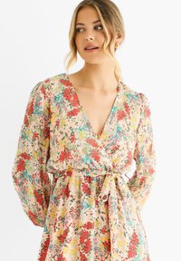 Blumen-Wickelkleid aus leichtem, strukturiertem Stoff mit roten, gelben und grünen Mustern. Tiefer V-Ausschnitt mit Puffärmeln und einer Taillenschnürung.
