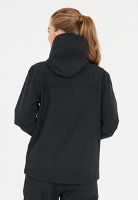 Svart utomhusjacka med huva, tillverkad av ett texturerat tyg och med en avslappnad passform. Ingen synlig hårdvara eller mönster, enkel design.