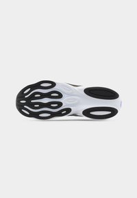 Suola di una sneaker bianca con motivi ovali neri sul battistrada, su uno sfondo grigio chiaro uniforme.