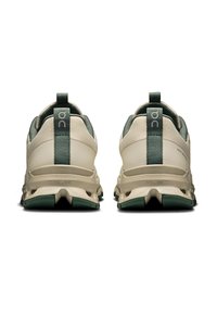 Beige Sport Schuhe mit einem grünen Akzentstreifen, gepolsterter Ferse und strukturiertem Sohlenprofil. Mit einem Zugband an der Ferse für einfaches An- und Ausziehen.